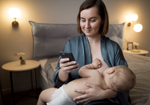 young-woman-breastfeeding-her-cute-baby-while-checking-her-phone
